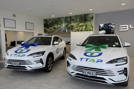 Two TTAP-branded electric vehicles in a dealership showroom, each with a ribbon across the bonnet on handover day.